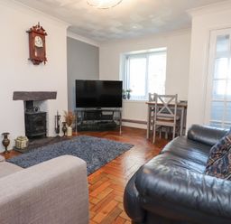 A living room with a black leather sofa a beige armchair a flat screen tv on a stand a small dining table with chairs and a wood burning stove at Tanyfron Holiday Studio in Bryngwran near Gwalchmai