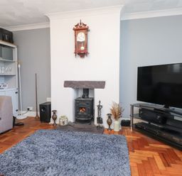 A living room with a fireplace clock television cabinet and gray rug at Tanyfron Holiday Studio Bryngwran near Gwalchmai