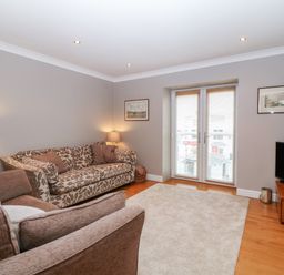 A living room with two sofas a television on a wooden stand and double doors with blinds at 10 Pen Llanw Tides Reach in Rhosneigr