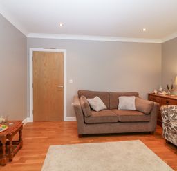 A living room with two sofas a wooden door two wooden tables and a lamp at 10 Pen Llanw Tides Reach in Rhosneigr