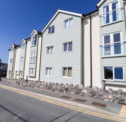 A street view of a residential building with multiple windows and stone wall at 10 Pen Llanw Tides Reach in Rhosneigr