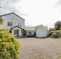 A white two-story house with attached garage and gravel driveway surrounded by bushes and trees at The White House in Cartmel