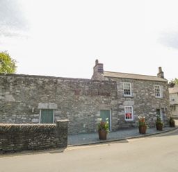 A stone building with green doors and four potted plants on a gravel area by a road at The White House in Cartmel