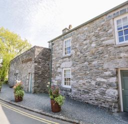 A stone building with potted plants outside along a gravel area at The White House in Cartmel