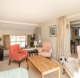 A sitting room with armchairs and a wooden table near a window with curtains at The White House in Cartmel