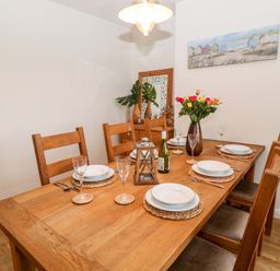 A wooden dining table set for six with plates glasses a bottle and a vase of flowers in a dining room at Cranberry in Bude