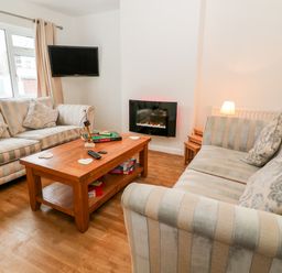 A living room with two striped sofas a wooden coffee table with game boxes and a wall-mounted television at Cranberry in Bude