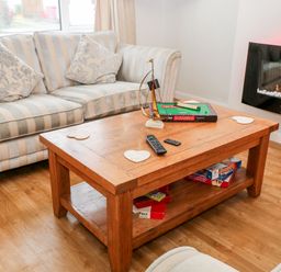 A living room with a striped sofa pillows a wooden coffee table with board games and remote controls and a wall-mounted electric fireplace Cranberry Bude