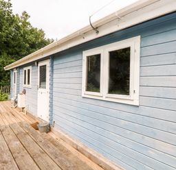 An exterior view of a blue wooden house with white windows and door on a wooden deck at The Beach Shack in Llansteffan