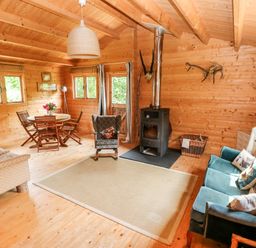 A wooden interior living room with a dining table and chairs a stove armchairs and a sofa at The Beach Shack in Llansteffan
