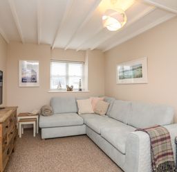 A living room with a light blue sectional sofa a wooden dresser with a tv two framed pictures and a window with blinds at The Granary - Rhoscolyn