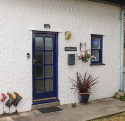 The front entrance of a white textured wall building with a blue door and window at The Granary in Rhoscolyn