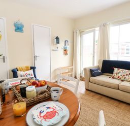 A living room with a beige sofa and a wooden dining table set with breakfast items at The Cranny in Mundesley