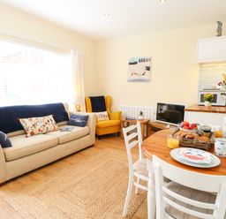 A living room with a beige sofa and yellow armchair and a dining table set with breakfast at The Cranny in Mundesley
