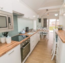 A kitchen with wooden countertops white cabinets a microwave stove kettle toaster and a dining table at Shore Thing 280 in Wilsthorpe