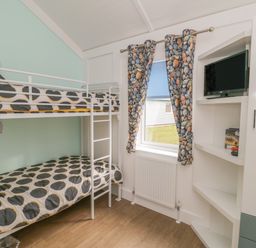 A bedroom with bunk beds and a TV mounted in shelves near a window with stone patterned curtains at Shore Thing 280 in Wilsthorpe