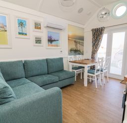 A living room with teal sofa white dining table and chairs framed beach pictures at Shore Thing 279 in Wilsthorpe
