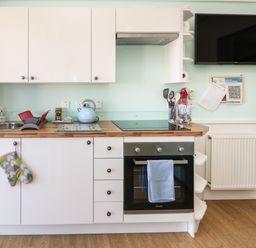 A kitchen with white cabinets wooden countertop oven and sink with a blue kettle a television mounted on the wall at Shore Thing 279 in Wilsthorpe