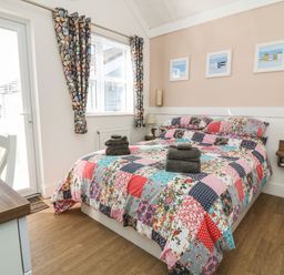 A bedroom with a double bed covered with a patchwork quilt and folded towels on top at Shore Thing 279 in Wilsthorpe
