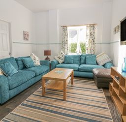 A living room with two blue sofas a wooden coffee table a striped rug and a wall mounted television at Gull Cottage in Tintagel