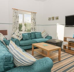 A living room with two teal sofas a wooden coffee table a wall-mounted television and a shelving unit at Gull Cottage in Tintagel