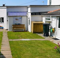 A backyard with a stone pathway wooden bench rainwater barrel and garden hose at Gull Cottage in Tintagel