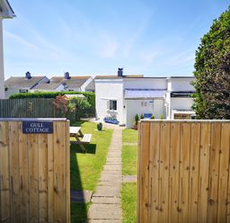 A garden path leading to a white cottage with a wooden fence and a picnic table at Gull Cottage Tintagel