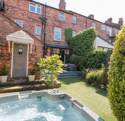 A backyard with a hot tub and patio furniture next to a brick house at Royal Victoria House in Scarborough