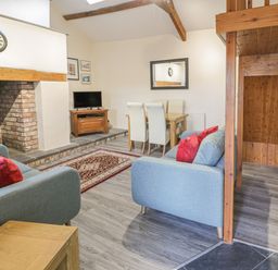 A living room with blue sofas red cushions a television on a wooden stand a dining table with four chairs and a fireplace at Crud yr Awel in Braichmelyn near Bethesda