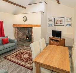 A living room with a wood burning stove a wooden dining table with four chairs a sofa with red cushions and wall art at Crud yr Awel in Braichmelyn near Bethesda