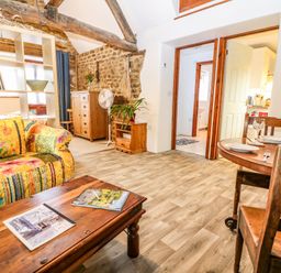 A living room with a wooden coffee table and a colorful sofa with a bookshelf behind at The Forge at Smithy Cottage in Bloxham
