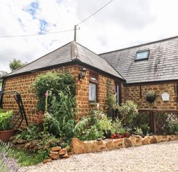 A stone cottage with a garden and potted plants outside at The Forge at Smithy Cottage in Bloxham