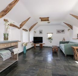 A living room with a green sofa a wooden side table a TV on a wooden stand and wooden ceiling beams at Harbour Cottage in Boscastle