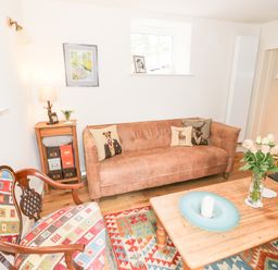 A living room with a brown sofa with animal cushions a patterned armchair a wooden coffee table with a vase of flowers and a candle near a brick fireplace at Prospect Cottage in Malvern Wells near Great Malvern