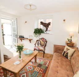 A living room with a brown sofa a wooden coffee table a colorful armchair and a patterned rug at Prospect Cottage Malvern Wells near Great Malvern