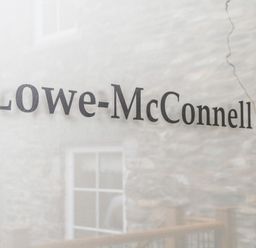 Text Lowe-McConnell on a translucent surface with a stone wall and window behind it at Lowe-McConnell in Far Sawrey