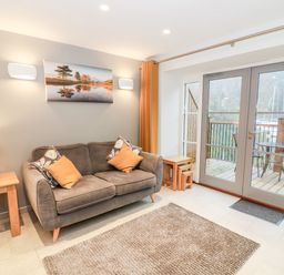 A living room with a sofa cushions table lamp and glass doors opening to a balcony at Lowe-McConnell in Far Sawrey