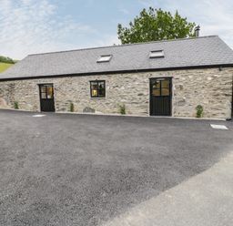 A stone building with two black doors and two windows on a paved area at The Shippon in Llanrwst