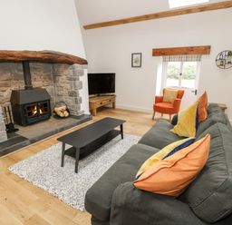 A living room with a stone fireplace a gray sofa with colorful cushions an orange armchair a black coffee table and a television at The Shippon in Llanrwst