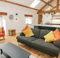 A living room with a gray sofa and colorful cushions next to an orange armchair and a kitchen with island and shelves at The Shippon in Llanrwst