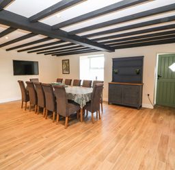 A dining room with a long table surrounded by chairs a television mounted on the wall a cabinet and a green door at Trewen in Botwnnog near Sarn Meyllteyrn