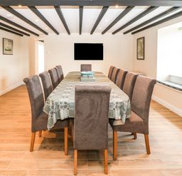 A dining room with a long table and twelve chairs under a ceiling with exposed wooden beams at Trewen Botwnnog near Sarn Meyllteyrn