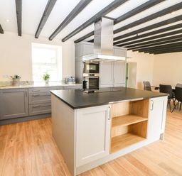 A kitchen with a central island, gray cabinets, a dining table with chairs, and exposed ceiling beams at Trewen in Botwnnog near Sarn Meyllteyrn