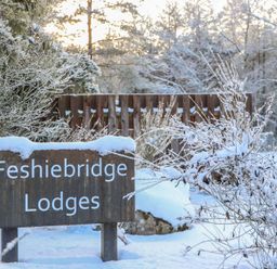 A sign for Feshiebridge Lodges surrounded by snow at Wildcat Lodge Feshiebridge near Aviemore