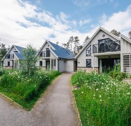 Three gray houses with black balconies surrounded by grass and flowers at Golden Eagle Lodge in Aviemore