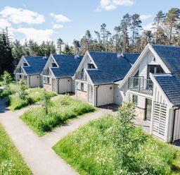 A row of white cabins with blue roofs and small balconies surrounded by grass and trees at Red Deer Lodge in Feshiebridge near Aviemore