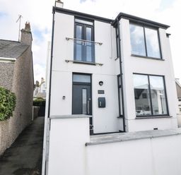 A modern two-story house with white walls large windows and black door at Arlanfor in Rhosneigr