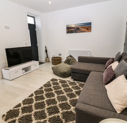 A living room with a gray sectional sofa, a patterned rug, a bean bag, a white TV stand with a television, and wall art at Arlanfor in Rhosneigr