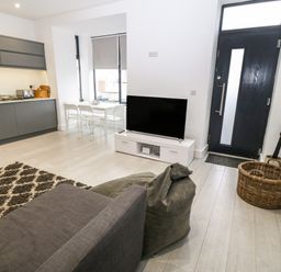 An open plan living space with a kitchen area dining table television sofa and black front door at Arlanfor in Rhosneigr