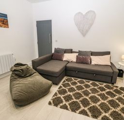 A living room with a gray sofa and pillows a bean bag chair a patterned rug a side table with a lamp and a wall decoration in the shape of a heart at Arlanfor in Rhosneigr
